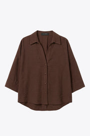Camisa de fit oversized, manga 3/4 amplia con doblez en puños, cuello camisero, escote v, pinza de amplitud en espalda con trabilla decorativa y bajo curveado. Cierre frontal con hilera de botones en contraste.