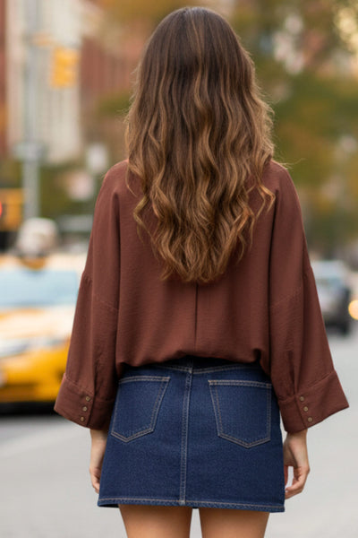 Camisa de fit oversized, manga 3/4 amplia con doblez en puños, cuello camisero, escote v, pinza de amplitud en espalda con trabilla decorativa y bajo curveado. Cierre frontal con hilera de botones en contraste.