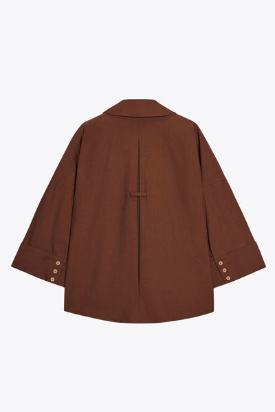 Camisa de fit oversized, manga 3/4 amplia con doblez en puños, cuello camisero, escote v, pinza de amplitud en espalda con trabilla decorativa y bajo curveado. Cierre frontal con hilera de botones en contraste.