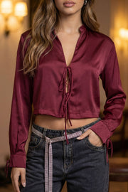 Blusa corta satinada de fit recto, manga larga con lazos en puños y cuello mock. Cierre frontal con lazos amarrables.