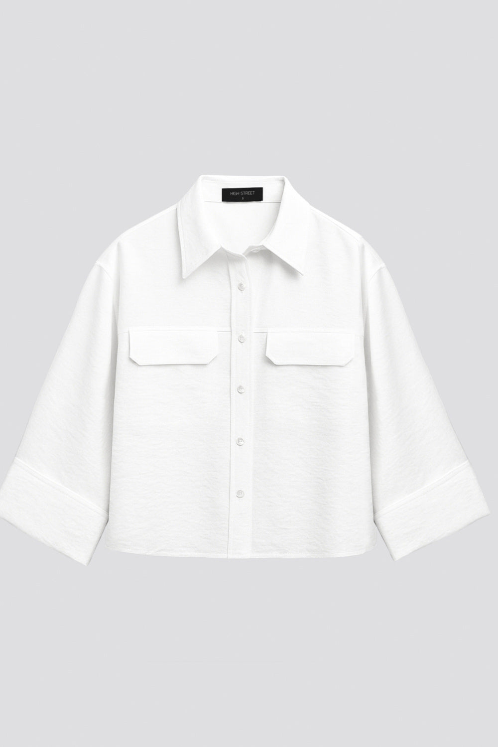 Camisa corta de fit oversized, manga 3/4 amplia con doblez en puños, cuello camisero, bolsillos frontales decorativos con cartera y pinza de amplitud en espalda. Cierre frontal con hilera de botones.