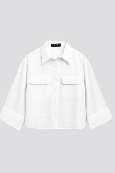 Camisa corta de fit oversized, manga 3/4 amplia con doblez en puños, cuello camisero, bolsillos frontales decorativos con cartera y pinza de amplitud en espalda. Cierre frontal con hilera de botones.