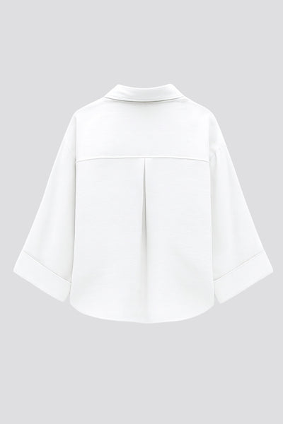 Camisa corta de fit oversized, manga 3/4 amplia con doblez en puños, cuello camisero, bolsillos frontales decorativos con cartera y pinza de amplitud en espalda. Cierre frontal con hilera de botones.