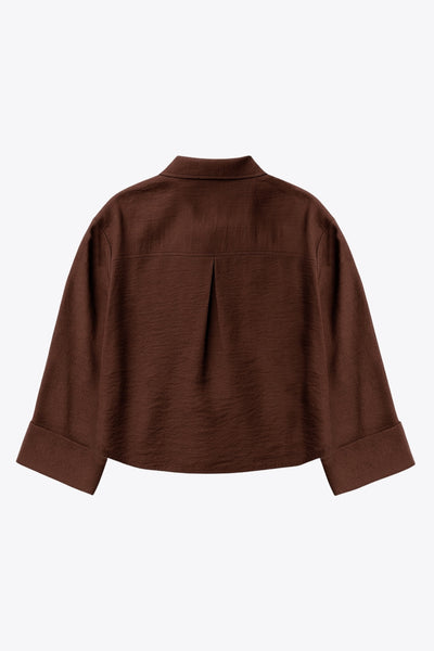 Camisa corta de fit oversized, manga 3/4 amplia con doblez en puños, cuello camisero, bolsillos frontales decorativos con cartera y pinza de amplitud en espalda. Cierre frontal con hilera de botones.