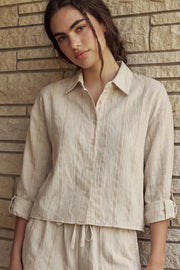 Camisa corta de rayas, ligeramente oversized, cuello camisero, manga larga rolled up con trabilla ajustable y botón. Cierre frontal con hilera de botones y detalle de pinza de amplitud en espalda.