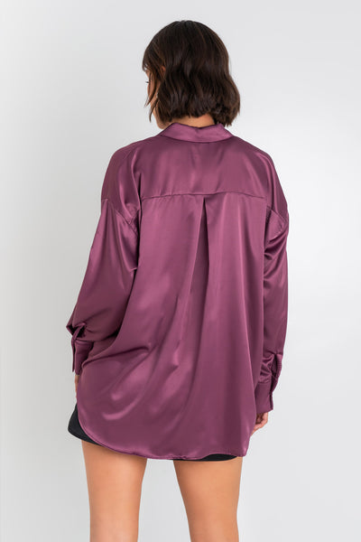 Camisa satinada de fit oversized, manga larga con puño abotonado, cuello camisero, bajo curveado, pinza de amplitud en espalda y cierre frontal con hilera de botones.