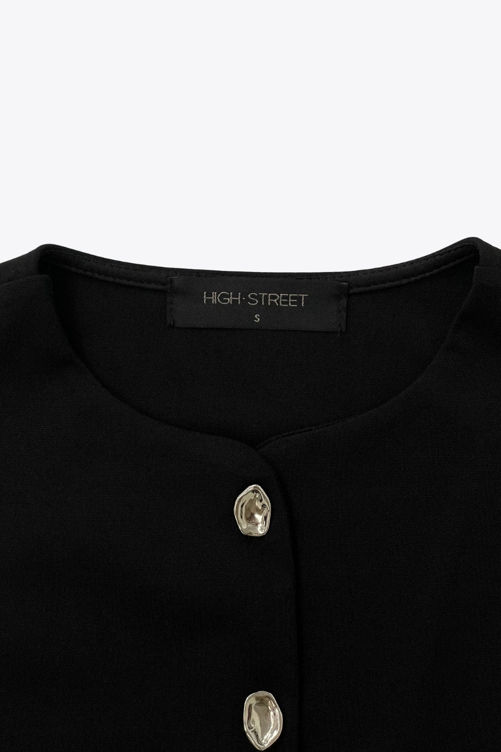 Chaleco corto de fit recto, cuello redondo y cierre frontal con hilera de botones en contraste. Detalle de abertura frontal en bajo.