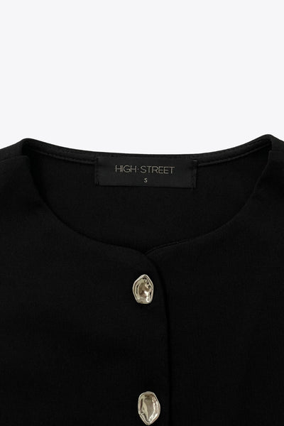 Chaleco corto de fit recto, cuello redondo y cierre frontal con hilera de botones en contraste. Detalle de abertura frontal en bajo.