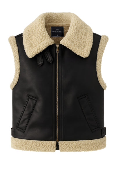 Chaleco corto de efecto piel, fit recto, cuello con solapa en contraste, bolsillos delanteros, trabillas laterales con hebillas en contraste y cierre frontal con cremallera. Detalle de borreguillo en contraste en interior, bordes y solapa.