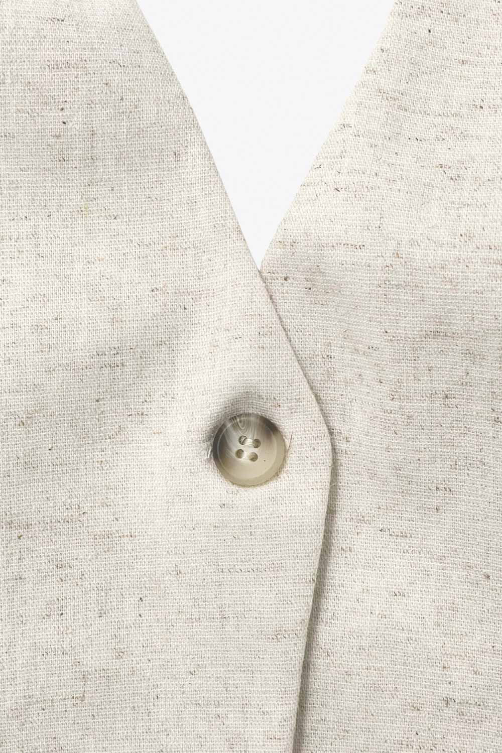 Chaleco corto de cuello halter con elástico posterior, fit ajustado, escote v, pinzas frontales, vivos decorativos frontales y bajo curveado. Cierre frontal con botón en contraste.