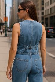 Chaleco corto de denim, escote v, pinzas con costuras frontales, vivos decorativos delanteros, trabilla posterior ajustable con hebilla y cierre frontal con hilera de botones.