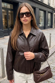 Chamarra de efecto piel, fit oversized, manga larga con puño abotonado, cuello solapa, bolsillos delanteros con vivos, costuras decorativas y elástico con plisados en bajo. Cierre frontal con cremallera oculta y botón.