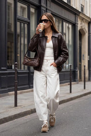 Chamarra de efecto piel, fit oversized, manga larga con puño abotonado, cuello solapa, bolsillos delanteros con vivos, costuras decorativas y elástico con plisados en bajo. Cierre frontal con cremallera oculta y botón.