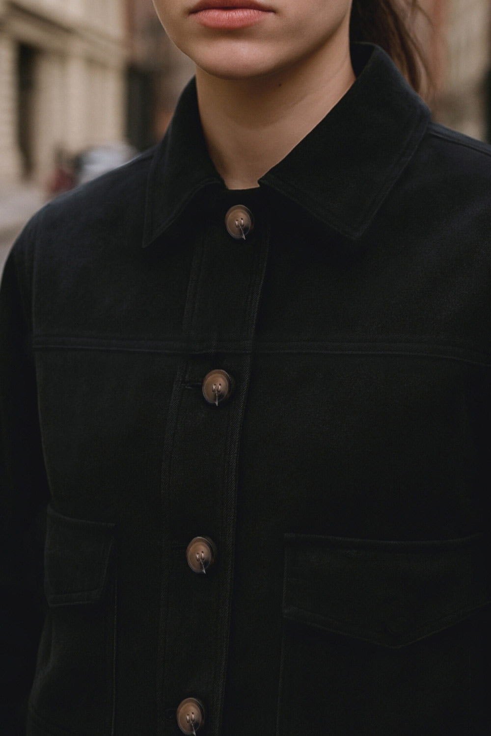 Chamarra corta fluida de gamuza, manga larga con puño abotonado, cuello camisero, bolsillos frontales de parche y cierre frontal con hilera de botones en contraste.