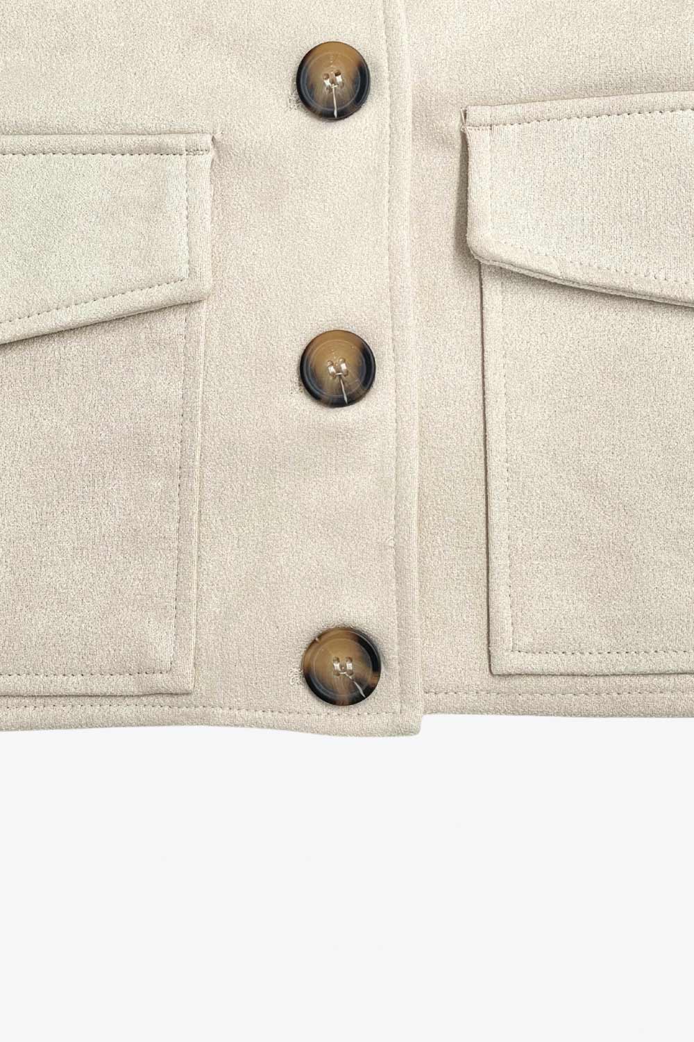 Chamarra corta fluida de gamuza, manga larga con puño abotonado, cuello camisero, bolsillos frontales de parche y cierre frontal con hilera de botones en contraste.