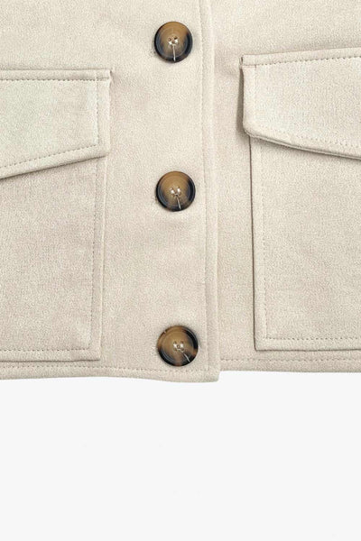 Chamarra corta fluida de gamuza, manga larga con puño abotonado, cuello camisero, bolsillos frontales de parche y cierre frontal con hilera de botones en contraste.