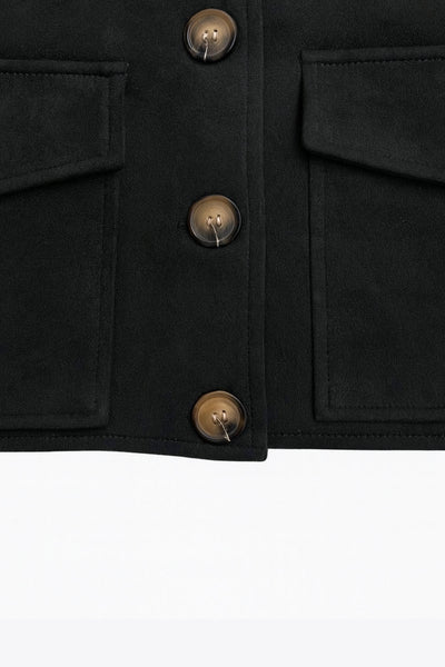 Chamarra corta fluida de gamuza, manga larga con puño abotonado, cuello camisero, bolsillos frontales de parche y cierre frontal con hilera de botones en contraste.