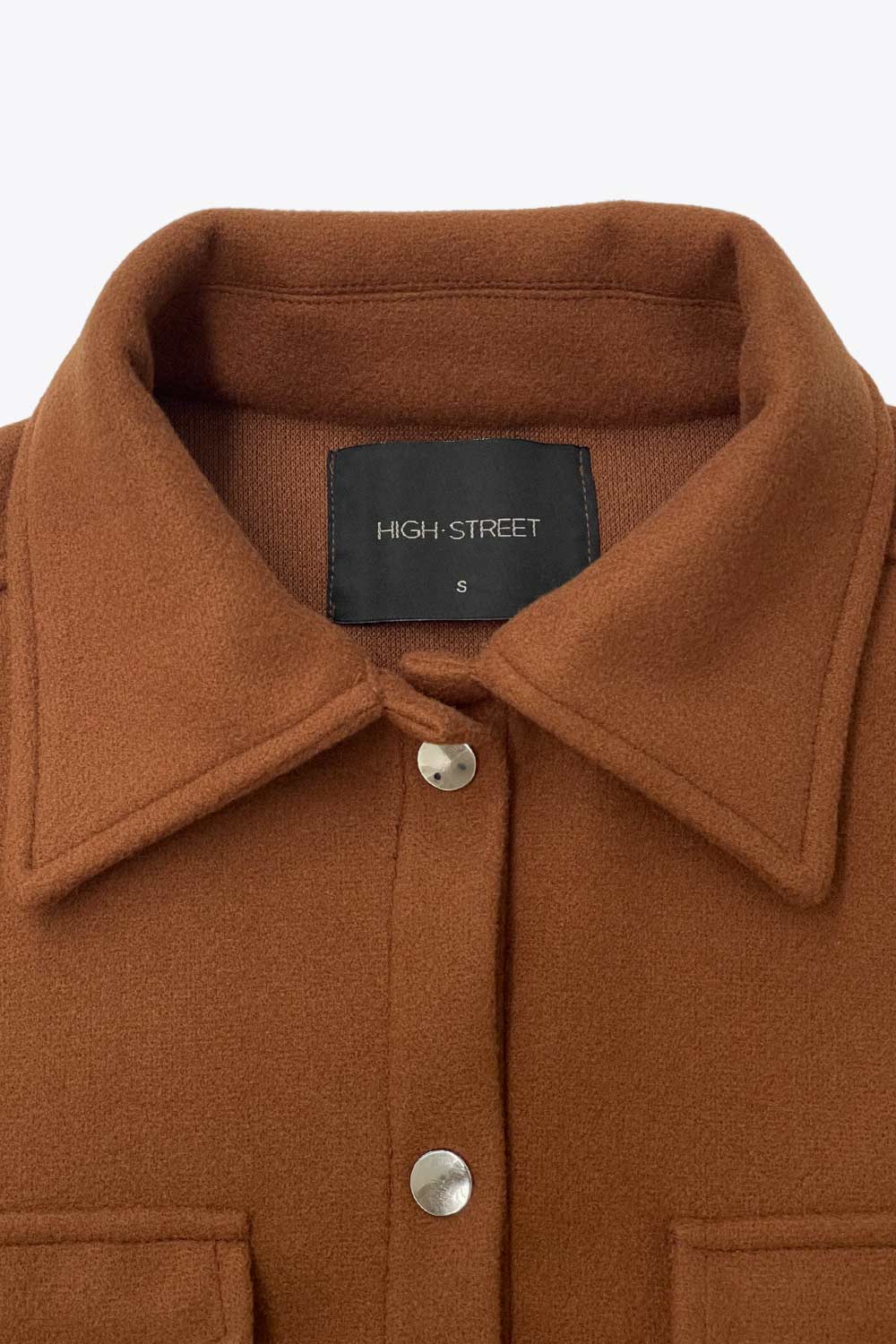 Chamarra corta de fit recto, cuello camisero, manga larga con puño abotonado, bolsillos delanteros con cartera, bajo curveado y cierre frontal con hilera de botones en contraste.