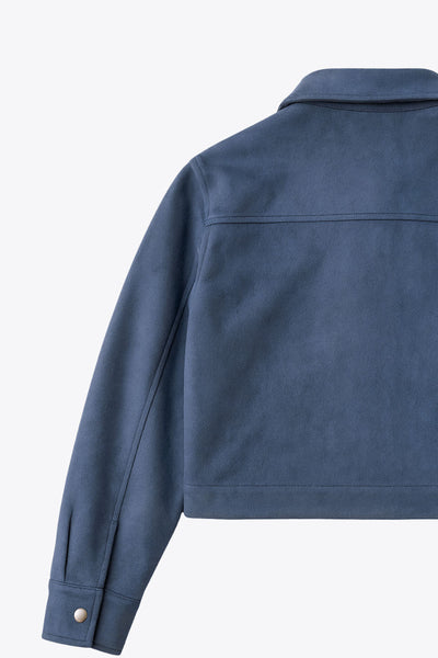 Chamarra corta de gamuza, fit recto, manga larga con puño abotonado, cuello camisero, bolsillos delanteros de parche con cartera y botones de presión. Cierre frontal con hilera de botones en contraste.