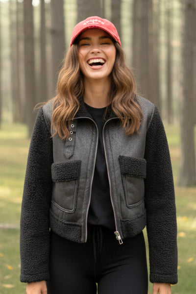 Chamarra corta de efecto piel, interior, mangas y cuello solapa de borreguillo, bolsillos delanteros de parche con detalle en contraste, fit recto, manga larga, costuras decorativas y cierre frontal con cremallera en contraste. Detalle de trabilla decorativa con hebilla en cuello.