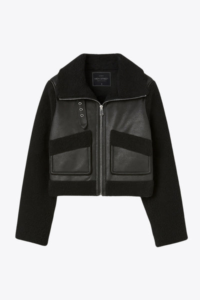 Chamarra corta de efecto piel, interior, mangas y cuello solapa de borreguillo, bolsillos delanteros de parche con detalle en contraste, fit recto, manga larga, costuras decorativas y cierre frontal con cremallera en contraste. Detalle de trabilla decorativa con hebilla en cuello.