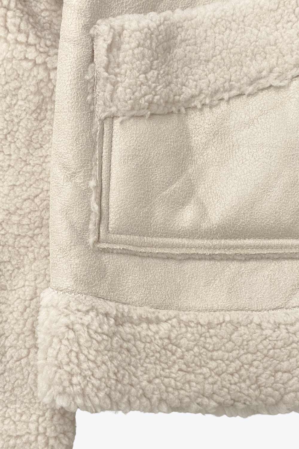 Chamarra corta de efecto piel, interior, mangas y cuello solapa de borreguillo, bolsillos delanteros de parche con detalle en contraste, fit recto, manga larga, costuras decorativas y cierre frontal con cremallera en contraste. Detalle de trabilla decorativa con hebilla en cuello.