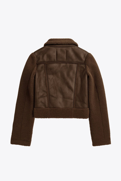 Chamarra corta de efecto piel, interior, mangas y cuello solapa de borreguillo, bolsillos delanteros de parche con detalle en contraste, fit recto, manga larga, costuras decorativas y cierre frontal con cremallera en contraste. Detalle de trabilla decorativa con hebilla en cuello.