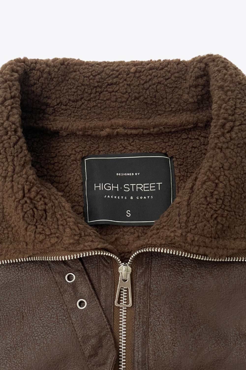 Chamarra corta de efecto piel, interior, mangas y cuello solapa de borreguillo, bolsillos delanteros de parche con detalle en contraste, fit recto, manga larga, costuras decorativas y cierre frontal con cremallera en contraste. Detalle de trabilla decorativa con hebilla en cuello.