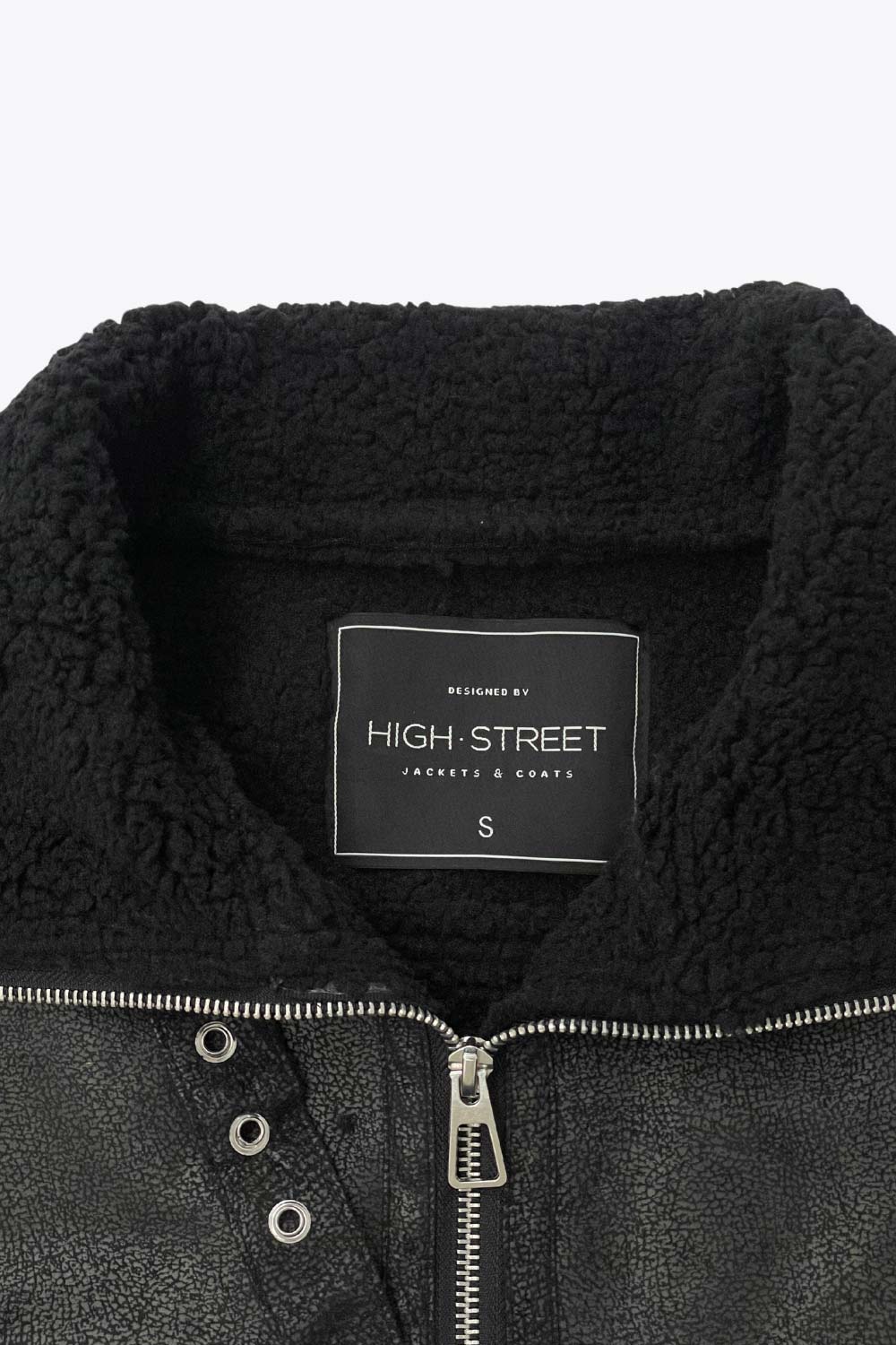 Chamarra corta de efecto piel, interior, mangas y cuello solapa de borreguillo, bolsillos delanteros de parche con detalle en contraste, fit recto, manga larga, costuras decorativas y cierre frontal con cremallera en contraste. Detalle de trabilla decorativa con hebilla en cuello.