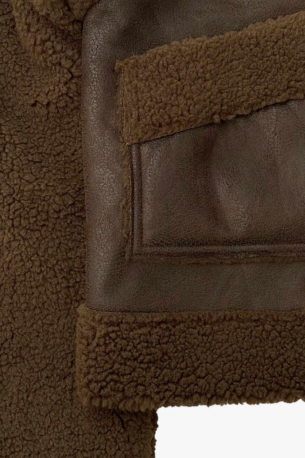 Chamarra corta de efecto piel, interior, mangas y cuello solapa de borreguillo, bolsillos delanteros de parche con detalle en contraste, fit recto, manga larga, costuras decorativas y cierre frontal con cremallera en contraste. Detalle de trabilla decorativa con hebilla en cuello.