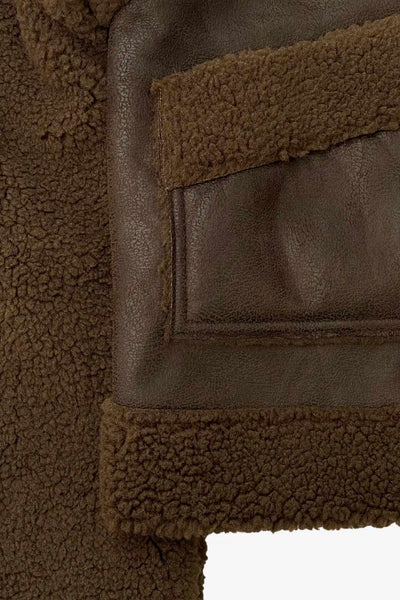 Chamarra corta de efecto piel, interior, mangas y cuello solapa de borreguillo, bolsillos delanteros de parche con detalle en contraste, fit recto, manga larga, costuras decorativas y cierre frontal con cremallera en contraste. Detalle de trabilla decorativa con hebilla en cuello.