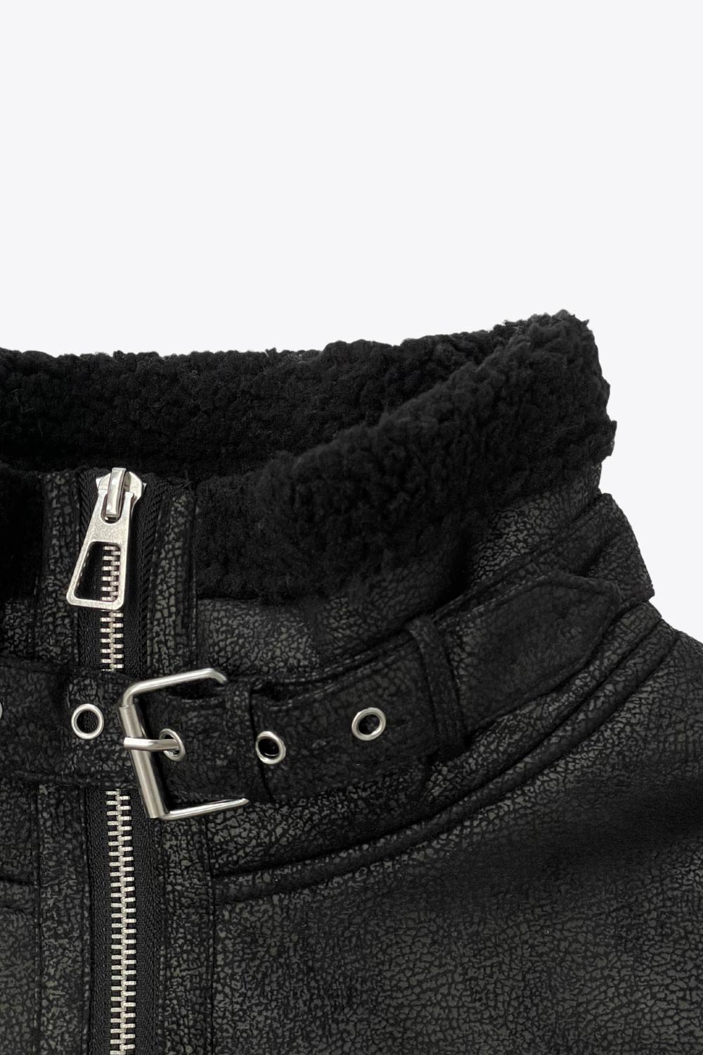 Chamarra corta de efecto piel, interior, mangas y cuello solapa de borreguillo, bolsillos delanteros de parche con detalle en contraste, fit recto, manga larga, costuras decorativas y cierre frontal con cremallera en contraste. Detalle de trabilla decorativa con hebilla en cuello.