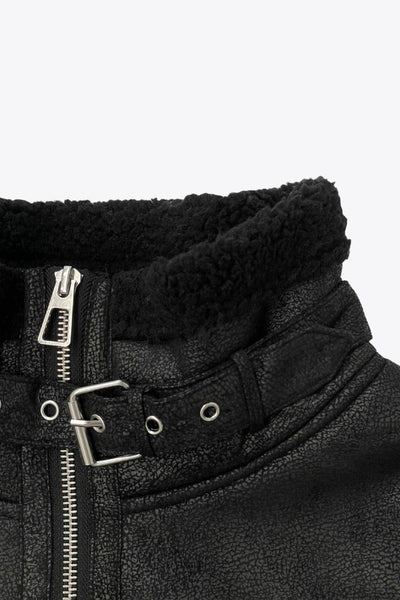 Chamarra corta de efecto piel, interior, mangas y cuello solapa de borreguillo, bolsillos delanteros de parche con detalle en contraste, fit recto, manga larga, costuras decorativas y cierre frontal con cremallera en contraste. Detalle de trabilla decorativa con hebilla en cuello.