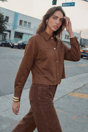 Chamarra corta de gamuza, fit oversized, cuello camisero, manga larga con puño abotonado, corte de bata frontal y posterior, bolsillos frontales de parche y cierre frontal con hilera de botones en contraste.