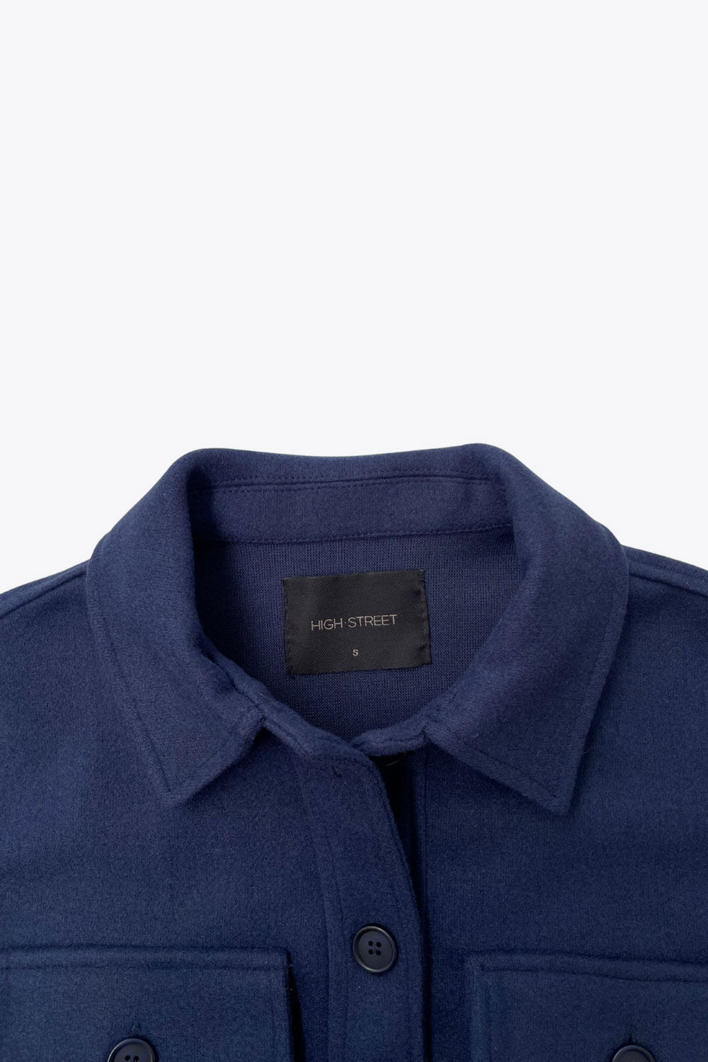 Chamarra corta de fit recto, cuello camisero, manga larga con puño abotonado, bolsillos delanteros de parche con cartera y botón en contraste. Cierre frontal con hilera de botones en contraste.