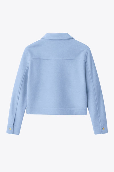 Chamarra corta de fit recto, cuello camisero, manga larga con puño abotonado, cortes decorativos frontales, bolsillos delanteros con cartera y botón. Cierre frontal con hilera de botones en contraste.