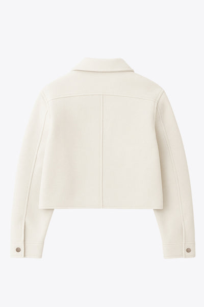 Chamarra corta de fit recto, cuello camisero, manga larga con puño abotonado, bolsillos delanteros con cartera y botón. Cierre frontal con hilera de botones en contraste.