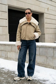 Chamarra corta de manga larga con puño, cuello solapa en contraste con borreguillo, bolsillos delanteros con cremallera y elástico con plisados en bajo. Cierre frontal con cremallera oculta.