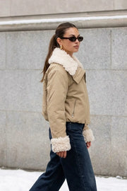 Chamarra corta de manga larga con puño, cuello solapa en contraste con borreguillo, bolsillos delanteros con cremallera y elástico con plisados en bajo. Cierre frontal con cremallera oculta.