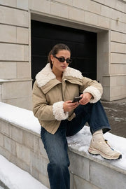 Chamarra corta de manga larga con puño, cuello solapa en contraste con borreguillo, bolsillos delanteros con cremallera y elástico con plisados en bajo. Cierre frontal con cremallera oculta.