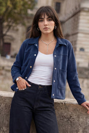 Chamarra corta de gamuza, fit recto, manga larga, cuello camisero, bolsillos delanteros de parche y cierre frontal con hilera de botones en contraste.