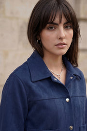 Chamarra corta de gamuza, fit recto, manga larga, cuello camisero, bolsillos delanteros de parche y cierre frontal con hilera de botones en contraste.