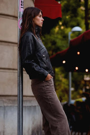 Chamarra de efecto piel, fit oversized, manga larga con puño abotonado, cuello alto, bolsillos delanteros con vivos y carteras, cortes decorativos y pretina elástica. Cierre frontal con cremallera oculta.