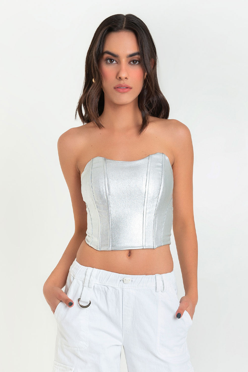 Woman in a silver crop top and white pants against a white background.