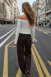 Crop top de fit ajustado, hombros descubiertos, manga larga, escote v con plisados y jareta ajustable, bajo frontal asimétrico con abertura frontal en v y costura decorativa. Detalle de rib rizado en bordes y textura de tejido.