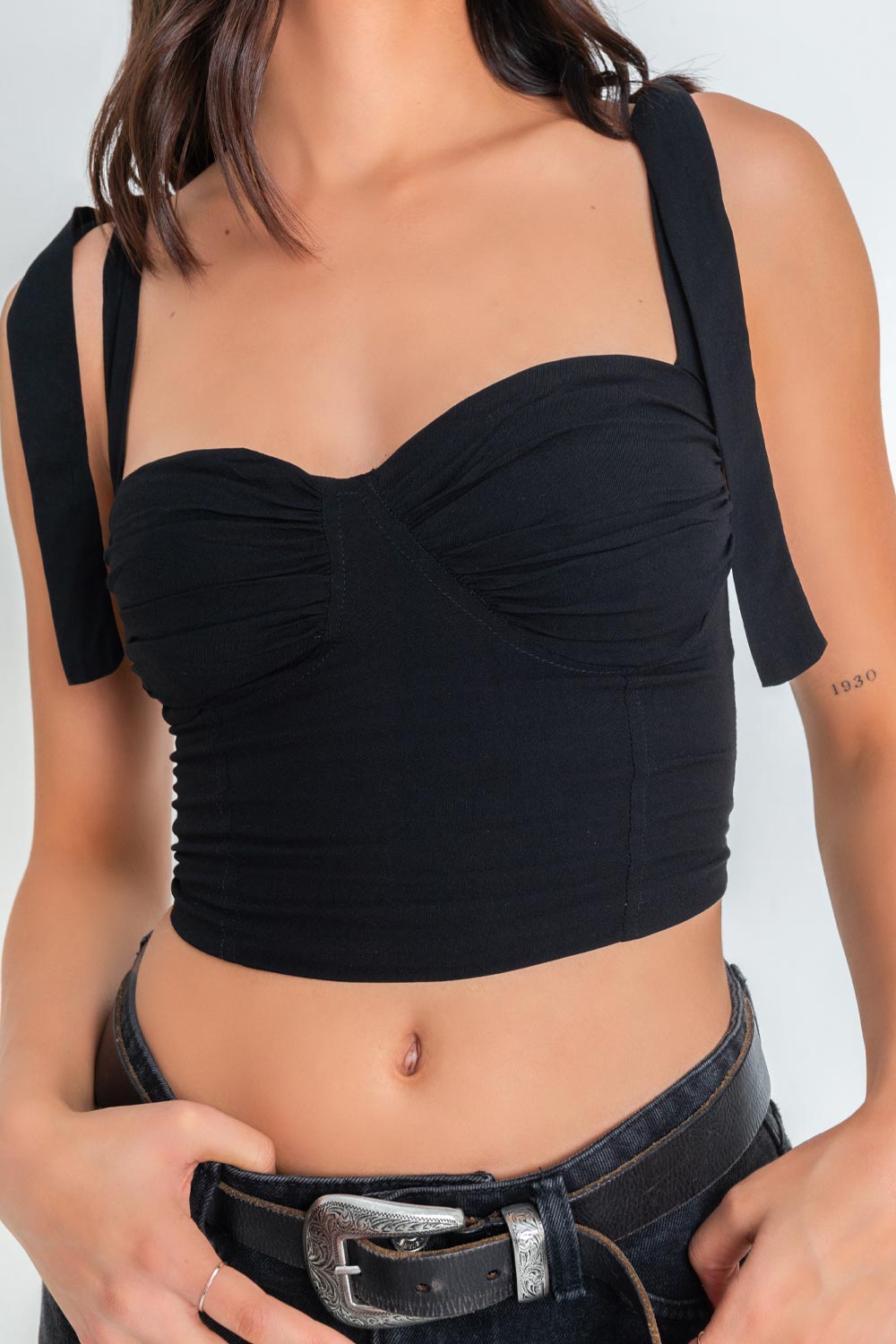 Crop top de fit ajustado, escote corazón con cortes decorativos y detalles plisados, costuras frontales y tirantes con nudo amarrable. Fruncido en espalda y cierre posterior con cremallera visible en contraste.