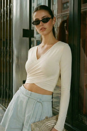 Crop top de escote v cruzado con plisados frontales, manga larga y fit ajustado.