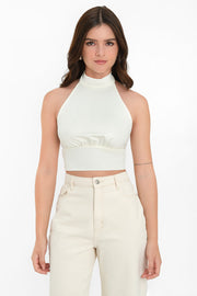 Crop top halter de cuello alto, sin mangas, escote espalda, plisados frontales con pretina, cierre posterior con botón, ojal y lazo amarrable inferior.