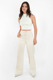Crop top halter de cuello alto, sin mangas, escote espalda, plisados frontales con pretina, cierre posterior con botón, ojal y lazo amarrable inferior.
