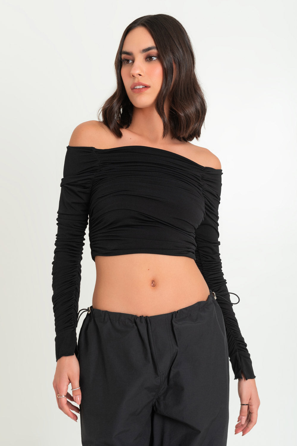 Crop top de fit ajustado, plisados en costados, hombros desubiertos, escote recto con plisados y manga larga plisada con abertura en puño. 